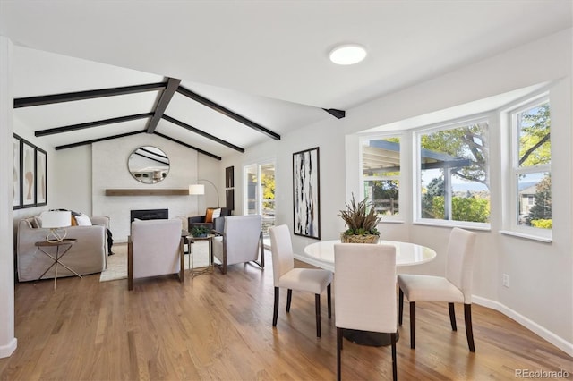 dining area with a large fireplace, light hardwood / wood-style floors, vaulted ceiling with beams, and a healthy amount of sunlight