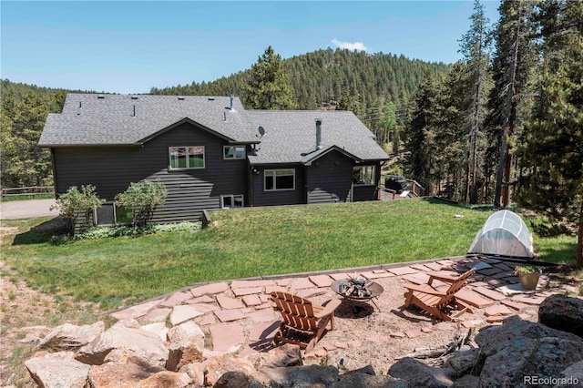 32663 Donna Dr, Conifer, CO 80433 - rear view of house featuring a fire pit, a forest view, roof with shingles, and a lawn