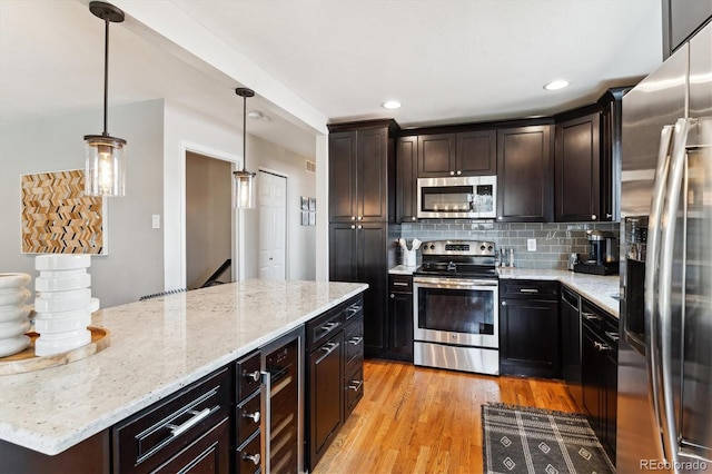 kitchen featuring light stone counters, light wood-style floors, decorative backsplash, beverage cooler, and appliances with stainless steel finishes