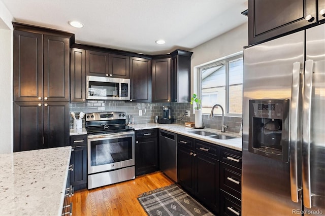 kitchen featuring tasteful backsplash, light wood-type flooring, light stone countertops, appliances with stainless steel finishes, and a sink