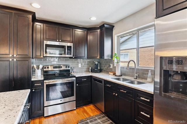 kitchen with a sink, light wood finished floors, light stone countertops, backsplash, and stainless steel appliances