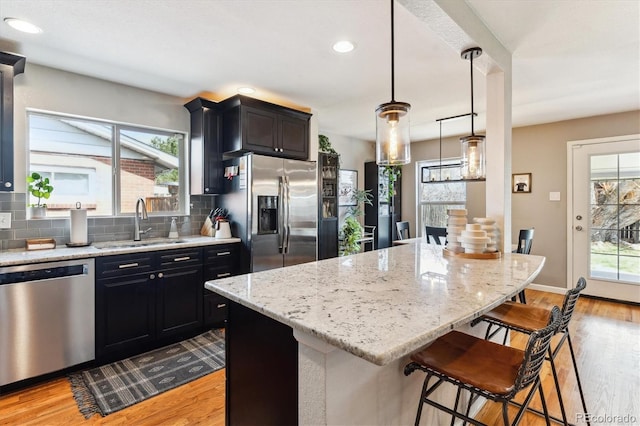 kitchen featuring light wood-style flooring, a sink, a breakfast bar, stainless steel appliances, and decorative backsplash