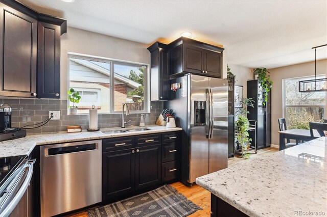 kitchen with a sink, backsplash, appliances with stainless steel finishes, and light stone counters