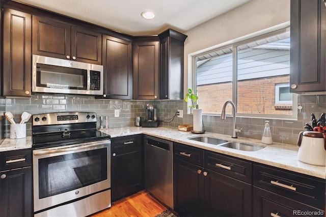 kitchen featuring light stone countertops, light wood-style flooring, a sink, stainless steel appliances, and backsplash
