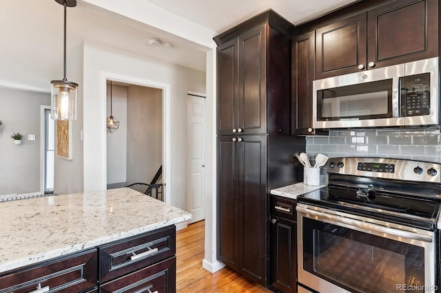 kitchen featuring light wood-style flooring, dark brown cabinets, light stone countertops, decorative backsplash, and appliances with stainless steel finishes