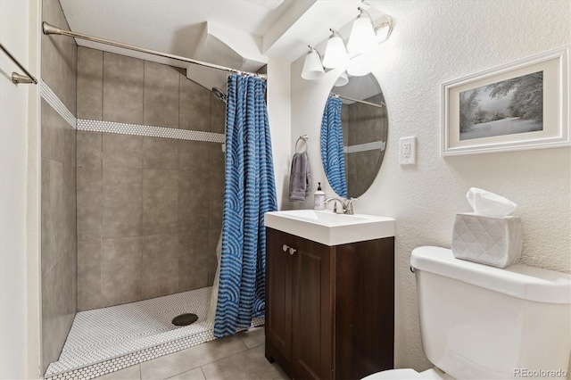 full bath featuring vanity, a textured wall, tile patterned flooring, toilet, and a tile shower