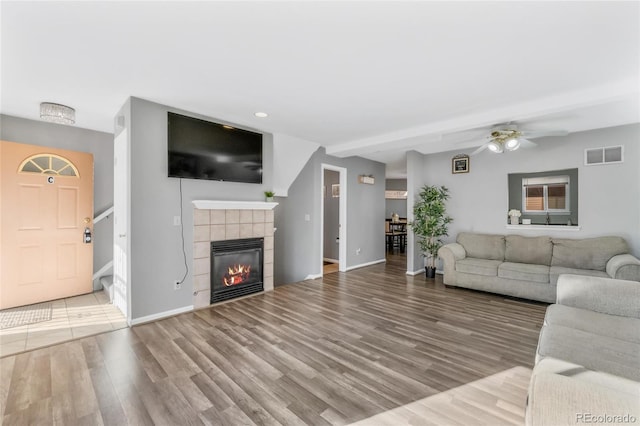 living room featuring ceiling fan, a tiled fireplace, and hardwood / wood-style floors