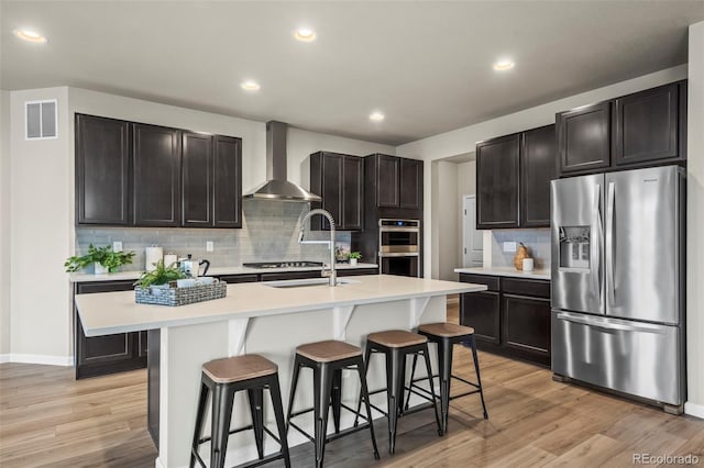 1677 Meagan Way, Erie, CO 80516 - kitchen featuring appliances with stainless steel finishes, wall chimney exhaust hood, a breakfast bar, tasteful backsplash, and a sink