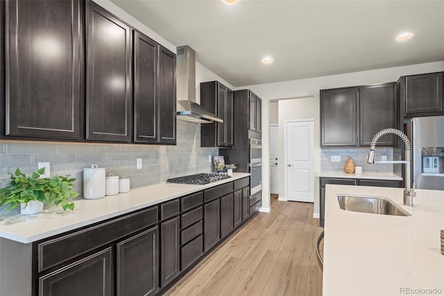 1677 Meagan Way, Erie, CO 80516 - kitchen with wall chimney range hood, stainless steel appliances, light wood-style flooring, a sink, and light countertops