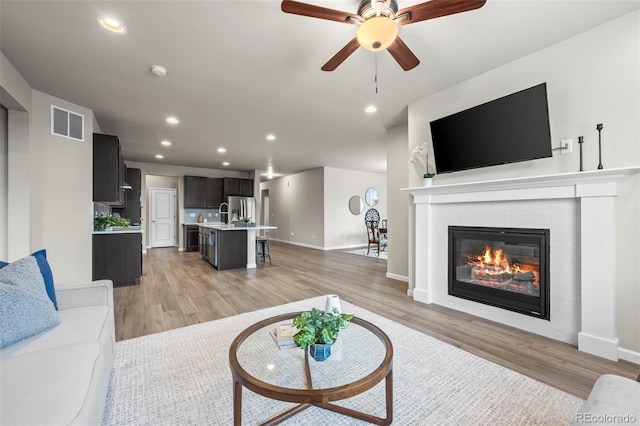 1677 Meagan Way, Erie, CO 80516 - living room featuring light wood finished floors, a brick fireplace, recessed lighting, a ceiling fan, and baseboards