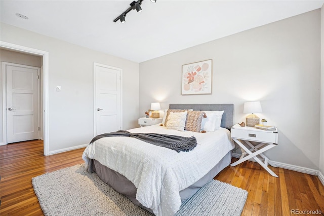 bedroom featuring rail lighting, wood finished floors, and baseboards