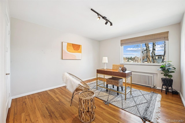 office area featuring rail lighting, radiator, wood finished floors, and baseboards