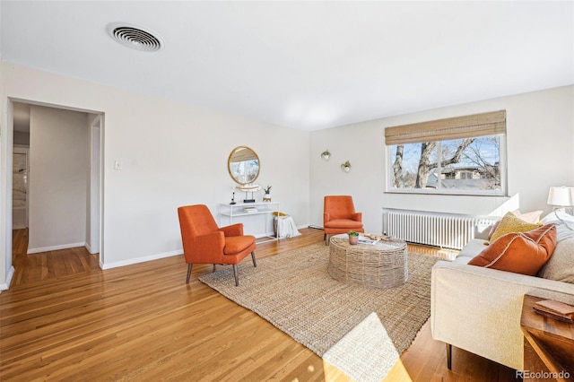 living room featuring visible vents, radiator, baseboards, and wood finished floors