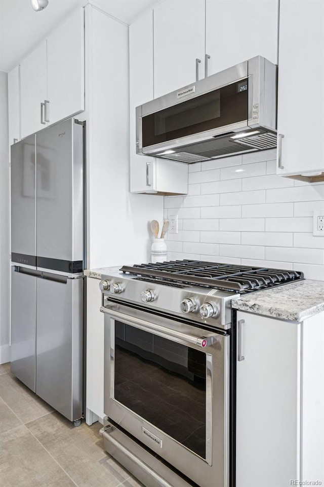 kitchen featuring tasteful backsplash, white cabinets, stainless steel appliances, and light stone countertops