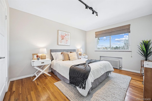 bedroom with rail lighting, baseboards, wood-type flooring, and radiator heating unit