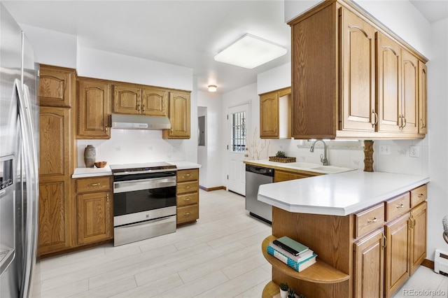 kitchen featuring appliances with stainless steel finishes, a sink, under cabinet range hood, light countertops, and brown cabinets
