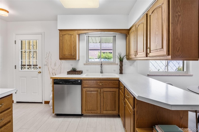 kitchen with dishwasher, a sink, light countertops, brown cabinets, and tasteful backsplash
