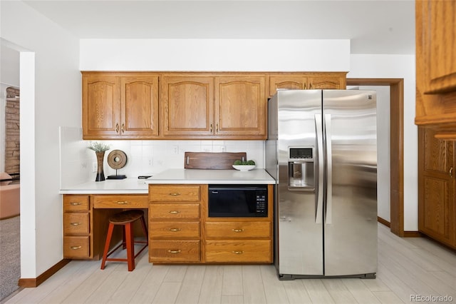 kitchen featuring stainless steel fridge, black microwave, backsplash, light countertops, and brown cabinets