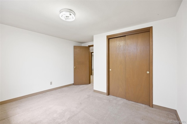 unfurnished bedroom with light colored carpet, a closet, and baseboards