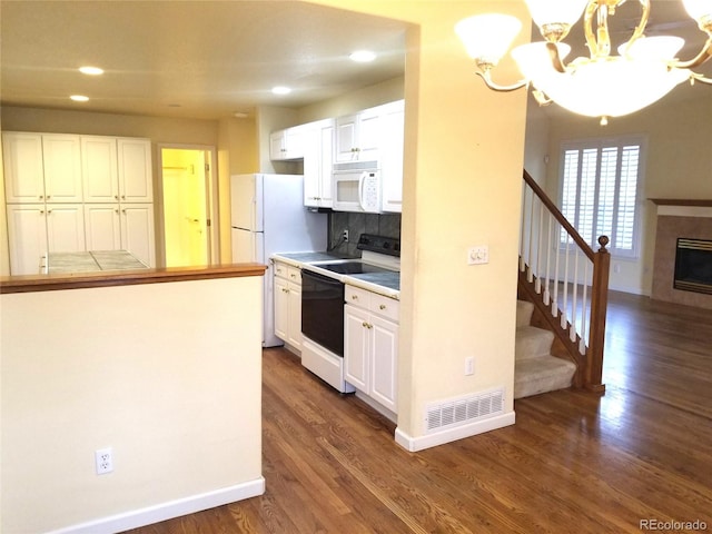 kitchen featuring white appliances, dark wood-type flooring, white cabinets, a fireplace, and a chandelier