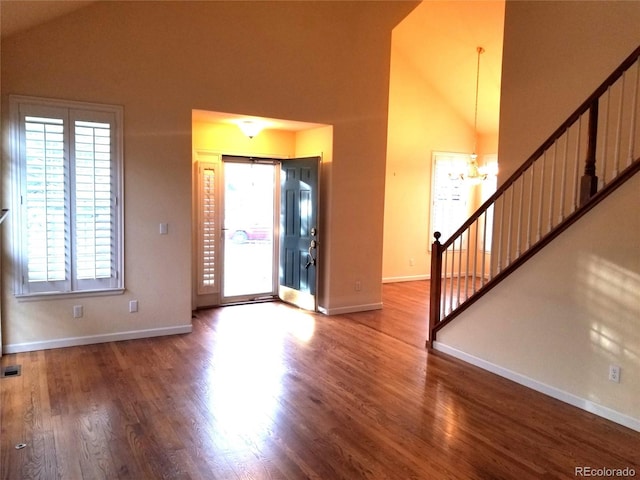 entrance foyer featuring high vaulted ceiling, a notable chandelier, stairway, and wood finished floors