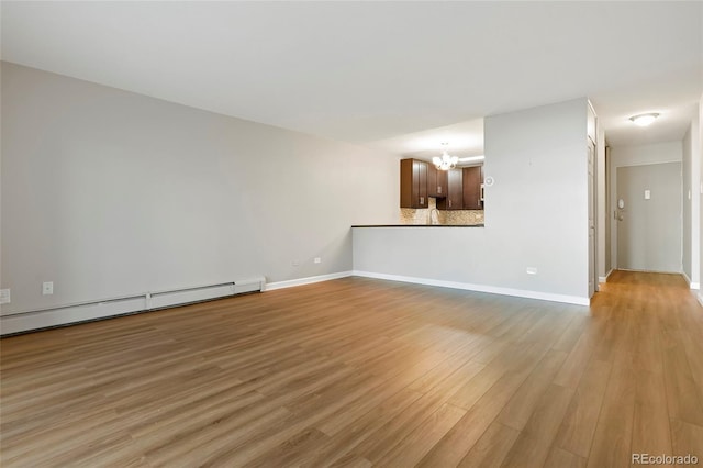 unfurnished living room featuring light hardwood / wood-style flooring, an inviting chandelier, and baseboard heating