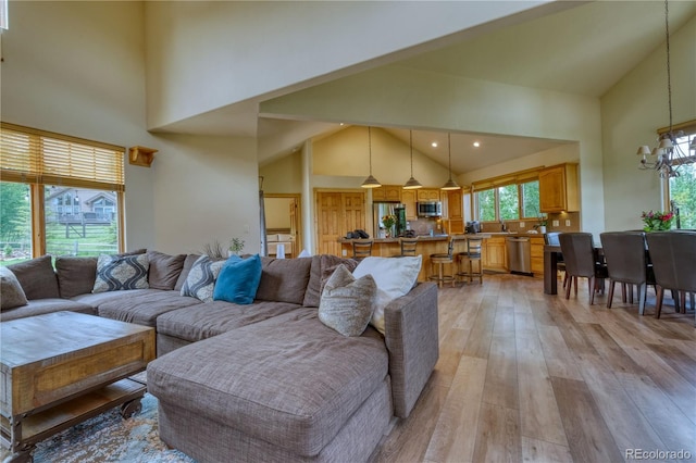 living room featuring high vaulted ceiling, a chandelier, and light wood-type flooring