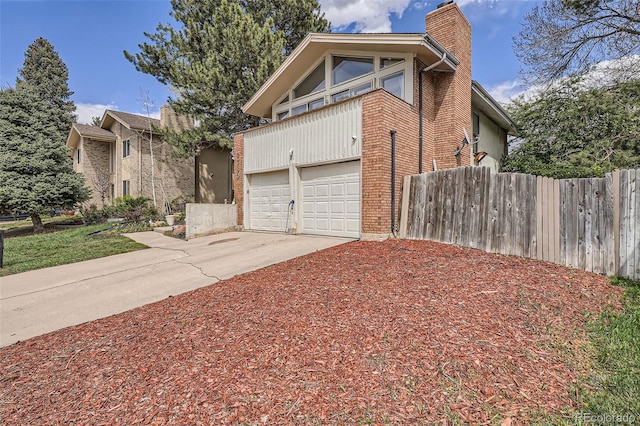 view of side of home with an attached garage, fence, a chimney, brick siding, and driveway