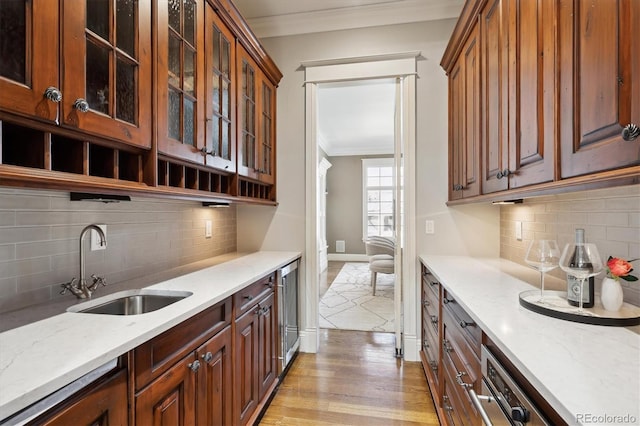 kitchen featuring glass insert cabinets, light stone counters, crown molding, light wood-style floors, and a sink