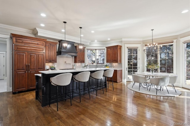 kitchen with a large island, custom range hood, a breakfast bar, decorative light fixtures, and light countertops