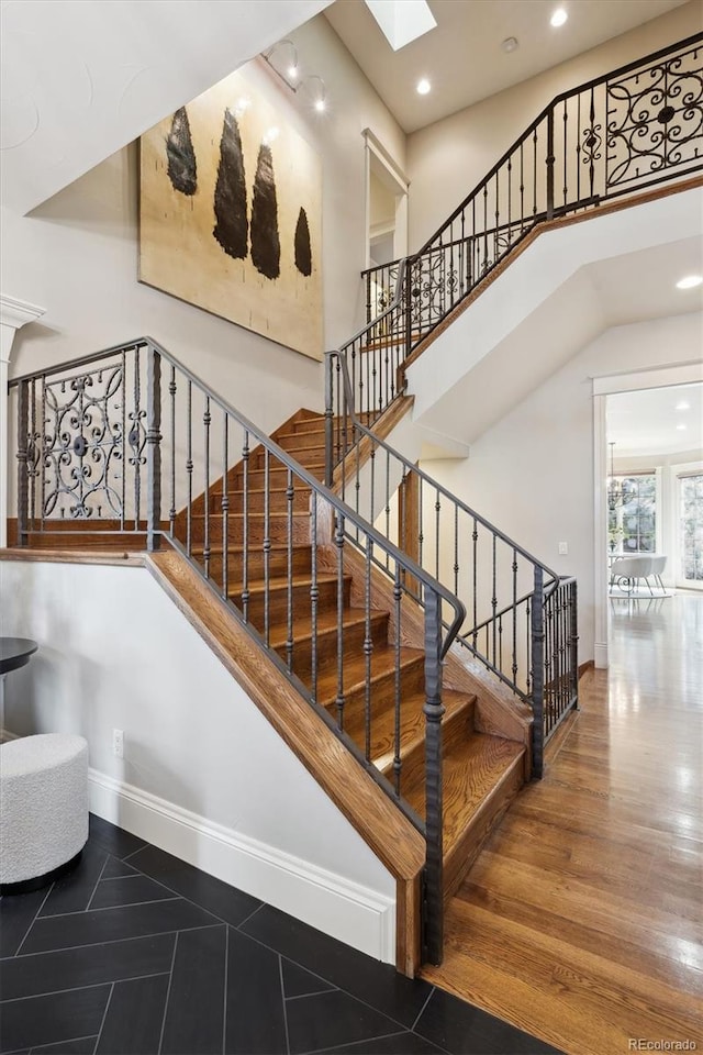 stairs featuring a skylight, recessed lighting, a high ceiling, wood finished floors, and baseboards