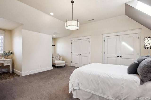 bedroom featuring baseboards, visible vents, vaulted ceiling, dark carpet, and two closets