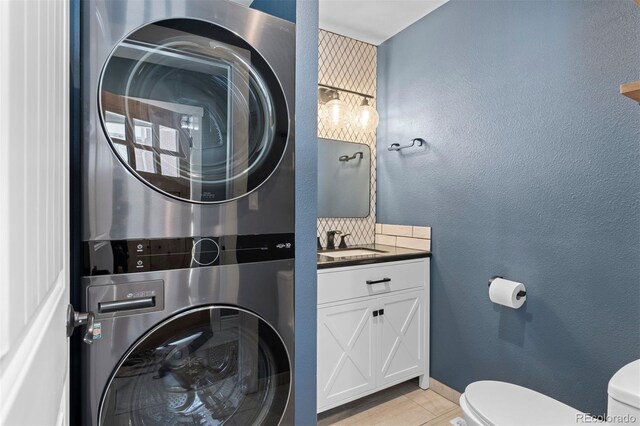 bathroom featuring a textured wall, vanity, toilet, and stacked washer / drying machine