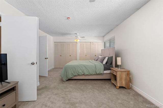 bedroom featuring baseboards, ceiling fan, light colored carpet, and multiple closets