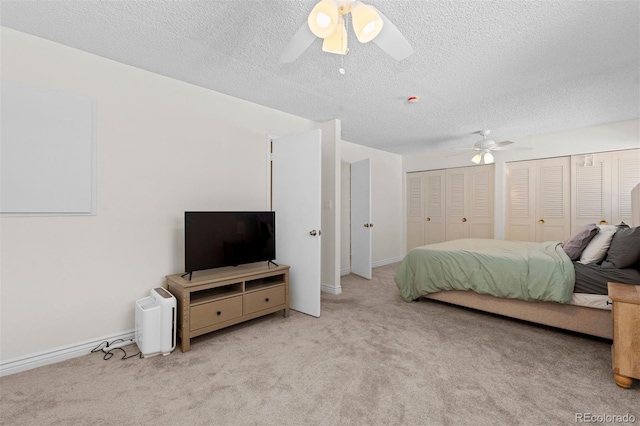 carpeted bedroom featuring a textured ceiling, ceiling fan, two closets, and baseboards