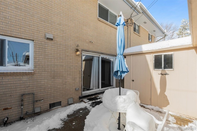 snow covered back of property featuring brick siding and crawl space