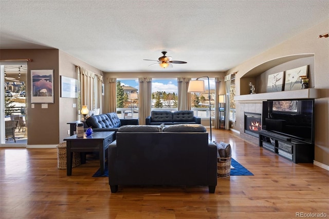 living room with a tile fireplace, hardwood / wood-style floors, ceiling fan, and a textured ceiling