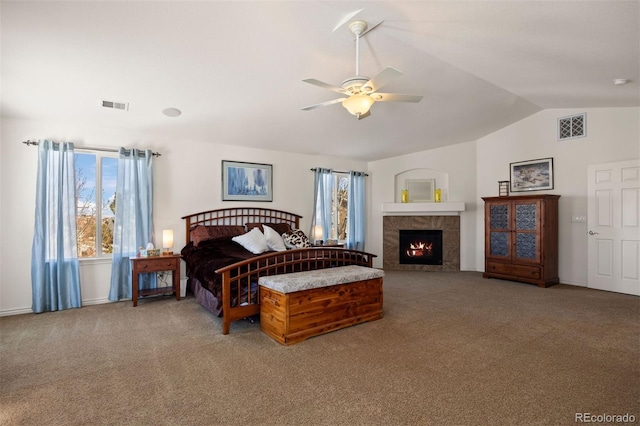 carpeted bedroom with a tile fireplace, vaulted ceiling, and ceiling fan