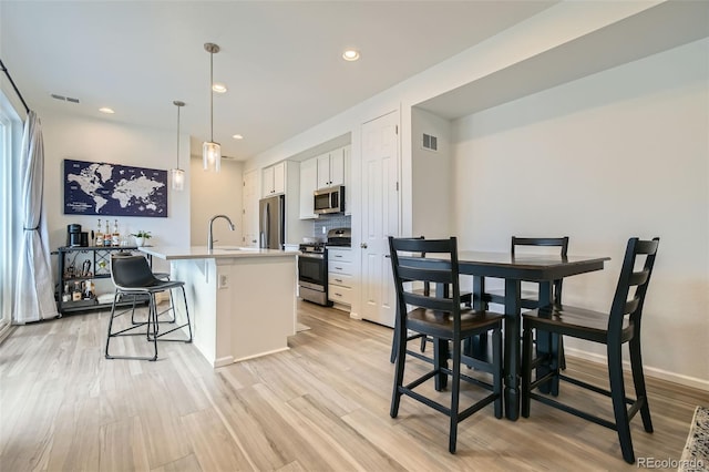 12345 Festival Ln, Thornton, CO 80241 - kitchen with stainless steel appliances, white cabinetry, an island with sink, light wood-type flooring, and a breakfast bar area