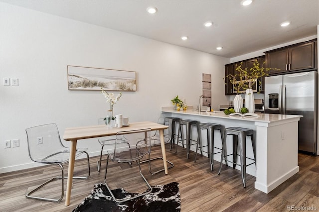 kitchen with light countertops, dark brown cabinets, a breakfast bar, a sink, and stainless steel fridge