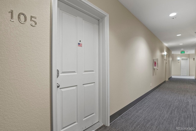 corridor with dark colored carpet, baseboards, recessed lighting, and a textured wall