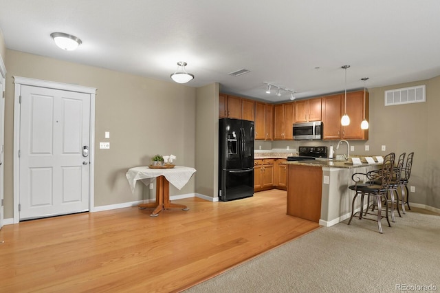 kitchen with sink, a breakfast bar, hanging light fixtures, black appliances, and kitchen peninsula