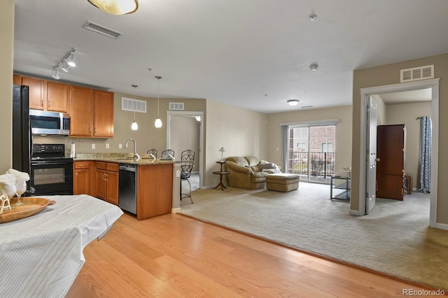 kitchen with a breakfast bar area, light hardwood / wood-style flooring, pendant lighting, light stone countertops, and black appliances