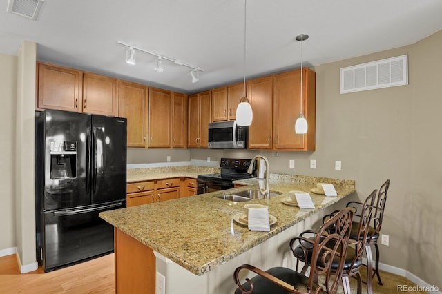 kitchen with pendant lighting, black appliances, sink, light stone counters, and kitchen peninsula