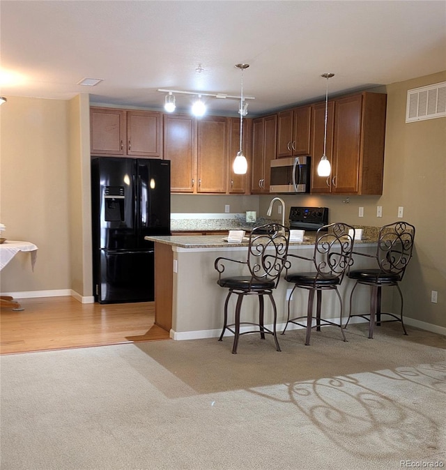 kitchen featuring visible vents, a peninsula, a kitchen breakfast bar, hanging light fixtures, and black appliances