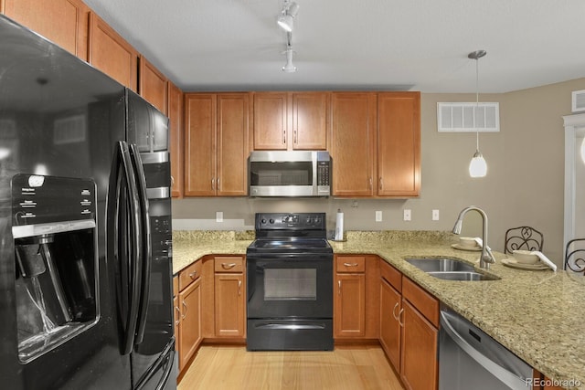 kitchen featuring visible vents, black appliances, a sink, brown cabinetry, and light stone countertops