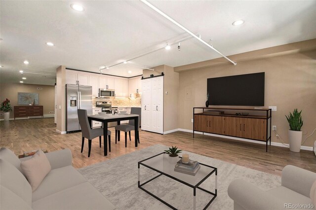 living room with a barn door, light wood-type flooring, and track lighting