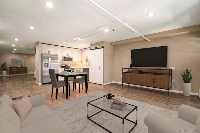 living room with a barn door, rail lighting, and light wood-type flooring