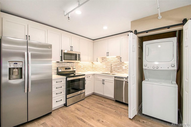 kitchen featuring a sink, stainless steel appliances, light countertops, white cabinetry, and stacked washer / dryer