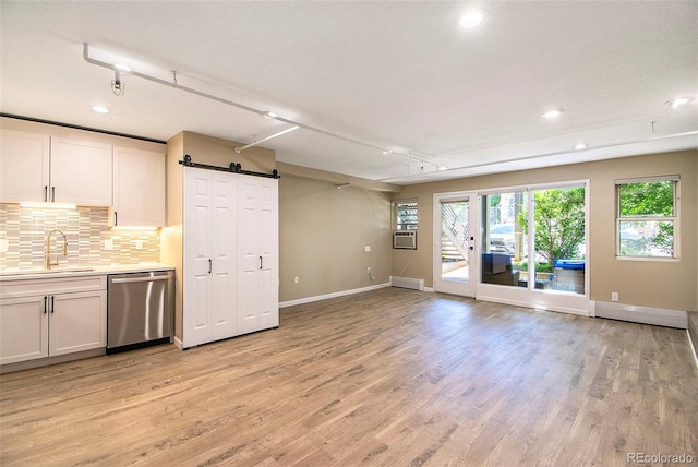 kitchen with sink, white cabinetry, tasteful backsplash, dishwasher, and a barn door